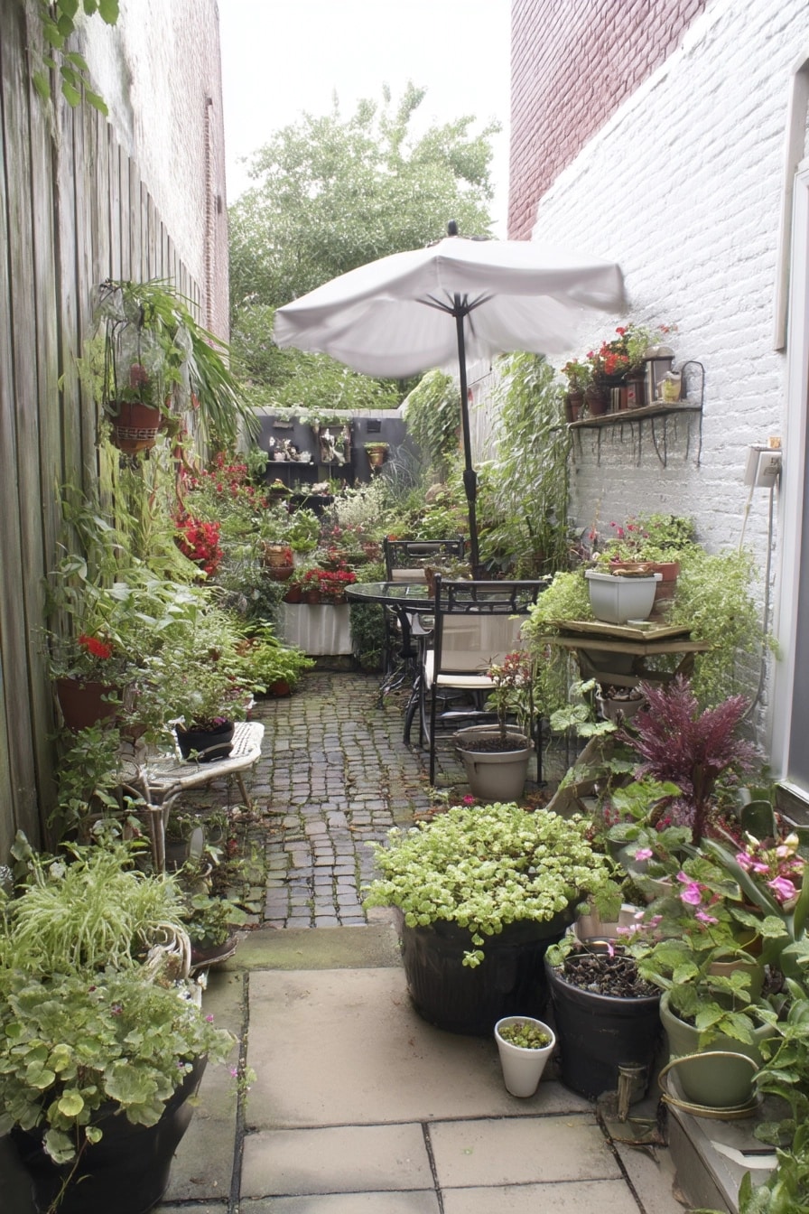 Very narrow brick-paved courtyard garden filled floor-to-ceiling with potted plants, wall shelves, and a small seating area under an umbrella at the end.